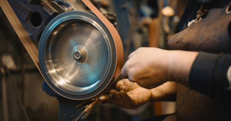 Craftsman uses a belt sander in machine shop. - obrazy, fototapety, plakaty