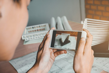 Architect using smart phone photograph model building in office.