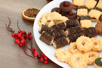 Detail photo of various homemade Christmas cookies, special Czech sweets; x-mas decoration background with cookies on white plate, festive arrangement with dried orange and red mistletoe