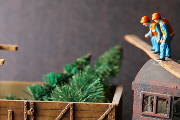 Miniature construction worker figure in action of look into wagon in the scene appear the tree model and train as a background also represent christmas event.