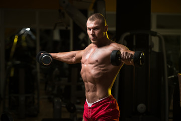 Fototapeta na wymiar Bodybuilder Exercising Shoulders With Dumbbells