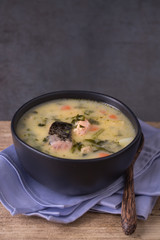 Seafood chowder in a black ceramic bowl placed on top of a blue cotton napkin. Dark background. Copy space. 