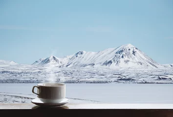 Rolgordijnen Cup of hot drink with steam on wooden desk and beautiful winter landscape view in the morning © SasinParaksa