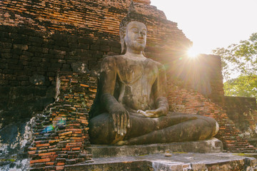Ancient sitting Buddha statue with sun flare in Sukhothai Historical Park,Thailand