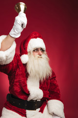seated santa claus rings his bell and looks to side