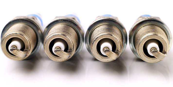 four brand new unused spark plugs on white background, suitable for header or banner
