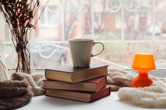 Coffee cup, stack of books, lantern and warm scarf on window siil with bokeh. Reading and rest concept.