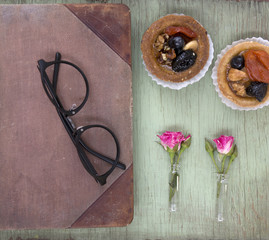 Vintage notebook mock up for artwork with pink roses and cakes. Place for text. Fresh flowers and black glasses.