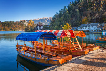 Bled, Slovenia - Traditional red, orange and blue Pletna boats in the autumn sunshine at Lake Bled with Bled Castle at background