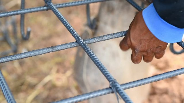 Workers hand holding wire and binding with steel by pliers at construction site
