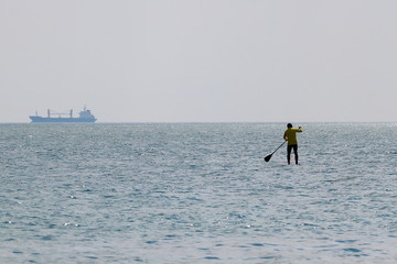 Silhouette of stand up paddle boarder paddling on a flat warm quiet sea
