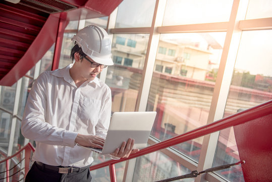 Young Asian Engineer or Architect working with laptop computer wearing a personal protective equipment safety helmet at construction site. Civil engineering; architecture and building project concepts