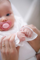 A newborn baby with a delicate pink skin lying on her mother's lap with a pink pacifier in her mouth, Mom gently holds the handle of her son, the child holds the pens in the cams