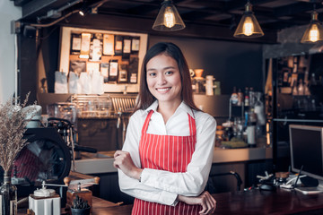 Asian female barista wear red apron crossed her arms at counter bar with smile face,cafe service concept,owner business start up