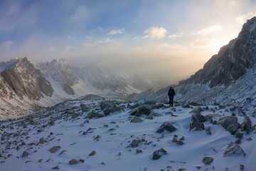 woman climber in helmet and down jacket with trekking sticks goes uphill at dawn