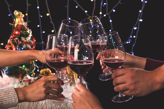 Friends celebrating Christmas or New Year eve party, cheering with wine, christmas lights decoration background, christmas atmosphere