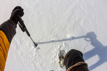 Tied climbers climbing mountain with snow field tied with a rope with ice axes and helmets first person