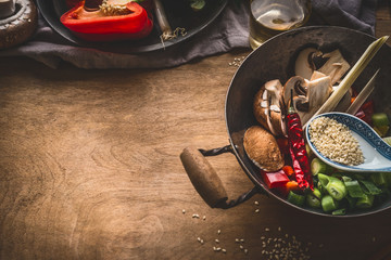 Wok pot with vegetarian asian cuisine ingredients for stir fry with chopped vegetables, spices, sesame seeds and lemongrass on rustic wooden background, top view. Chinese or Thai food cooking concept