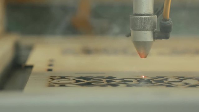 Machine for laser cutting wood close up cuts chipboard and the smoke appears. The red beam.