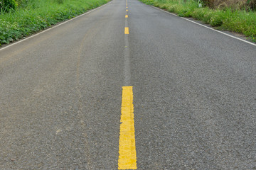The yellow line on concrete road with green grass beside on  this way