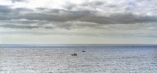 Panoramic view of two fishing boats fishing at the entrance of the bay of La Coruna on the coast of Galicia (Spain). Sky with clouds with sun reflections