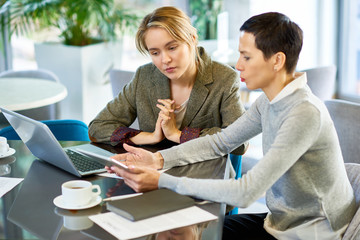 Portrait of two businesswomen discussing work and using laptop during business meeting in modern...