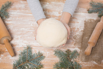 hands of a girl kneading dough on a wooden board, rolling pin, branches of a Christmas tree on a table