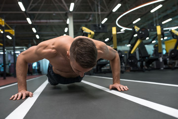 Fototapeta premium Portrait of young muscular man doing pushups on floor during workout in modern gym