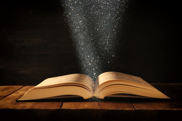 image of open antique book on wooden table with glitter overlay.