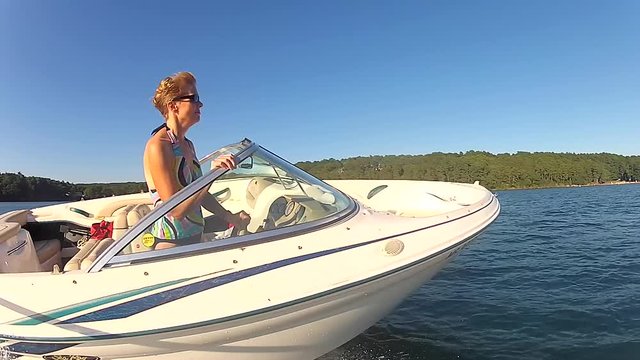 Riding along side speed boat on lake in summertime with woman driving