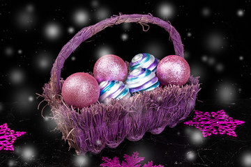 Christmas balls in purple basket on black background with snow. Decorative snowflakes.