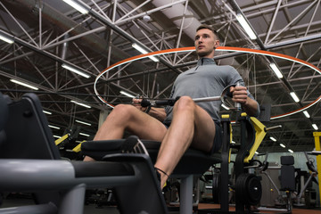 Fototapeta na wymiar Low angle portrait of handsome sportsman exercising using machines working out in modern gym