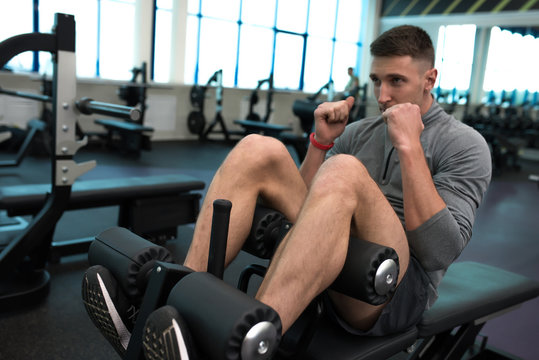 Portrait of handsome muscular man doing crunches on stand during work out in modern gym