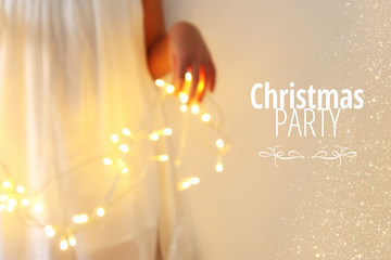 Abstract and bokeh image of young woman holding garland christmas lights and typography: CHRISTMAS PARTY. Holiday invitation concept.