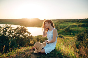 Young girl in a white dress with a hat and a wonderful sunset