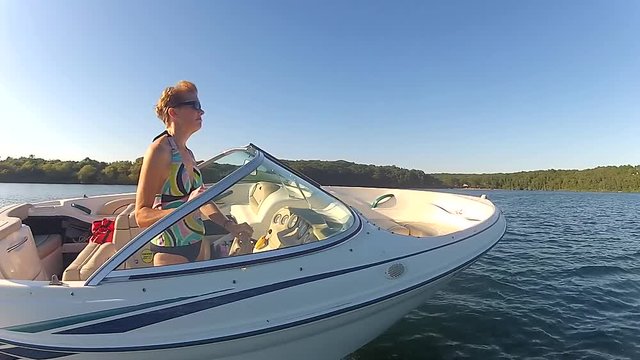 Riding along side speed boat on lake in summertime with woman driving