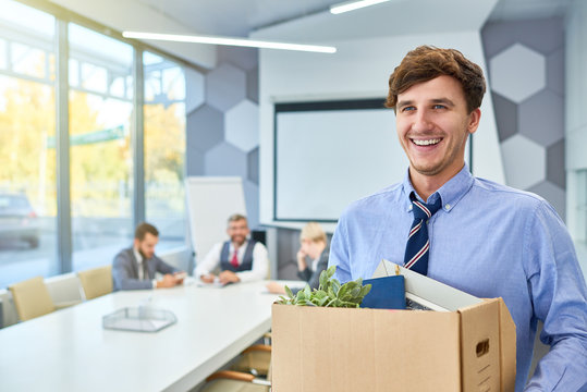 Portrait of happy young man holding box of personal belongings being hired to work in business company, copy space