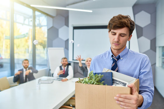 Portrait of sad young man holding box of personal belongings being fired from work in business company, copy space