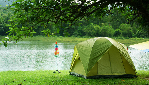 nature landscape green camping tent with colorful umbrella under the tree and blue with yellow tarp on meadow with lake or river and tree mountain for holiday relax on winter and gray sky at ched khot