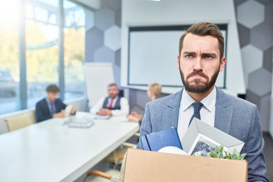 Portrait of sad bearded businessman holding box of personal belongings being fired from work in company, copy space