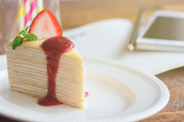 Delicious crepe cake on white plate decorated with mint served with strawberry sauce on wood table so soft sweet and sour. Homemade bakery concept of french dessert for birthday cake or cafe.