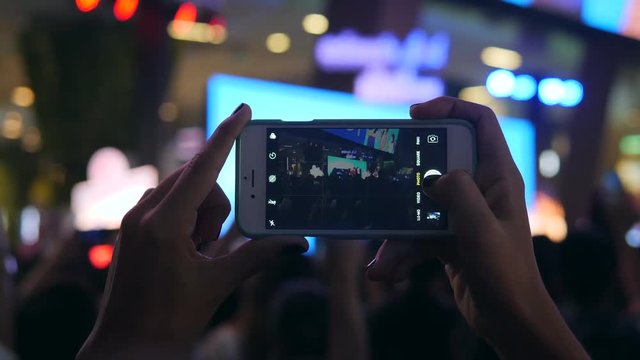 Womans Hands Holding Mobile Phone and Taking Photo of Concert Stage. Blured Blue Bokeh Pop Music Session Concept. 4K, Slowmotion. Bangkok, Thailand.