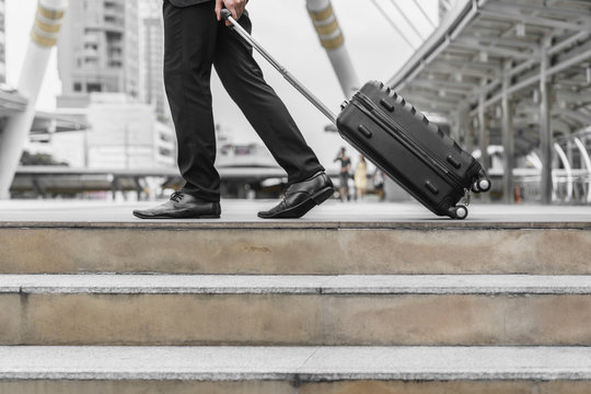Businessman drag luggage and hold suit in city outdoor on building background. Concept of business trip and work life balance.