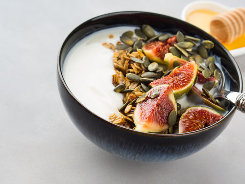 Healthy breakfast natural yogurt bowl with home made granola, pumpkin seeds and figs on gray background