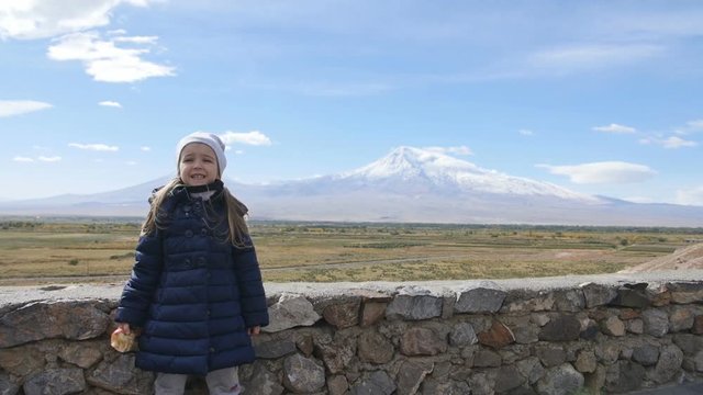 Portrait of vacation travel little girl looking at Ararat mountain landscape. Nature during summer vacations. Young kid standing at lookout looking at camera.