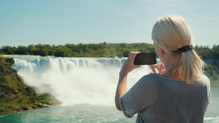 Vacation in Canada. A woman tourist takes pictures of the famous Niagara Falls. It stands on the Canadian shore, from where the waterfall is clearly seen