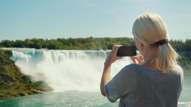 Vacation in Canada. A woman tourist takes pictures of the famous Niagara Falls. It stands on the Canadian shore, from where the waterfall is clearly seen