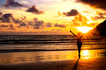 Silhouette of young girl with a hat looking far away at sunset on a beach.