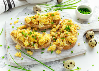 Homemade Quail Scrambled eggs on crispy toast, bread with green onion, chives on white board.