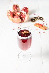Wineglass with alcohol pomegranate drink with spices over wooden table